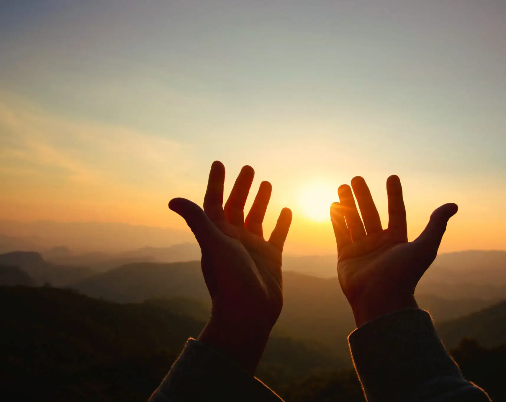 Hands cupping sunrise over mountain landscape