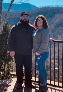 Couple posing outdoors with mountains in background.