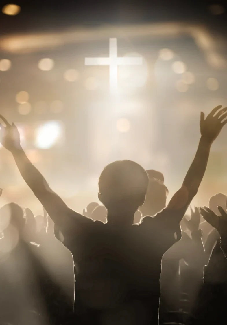 People worshiping with raised hands, cross visible.
